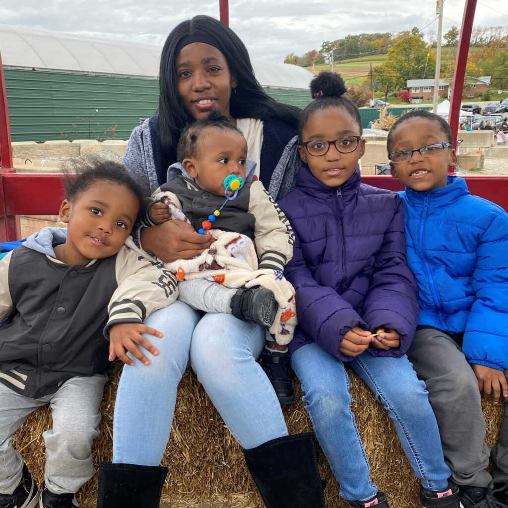 A Black mother sitting on hay bales with her four young children.